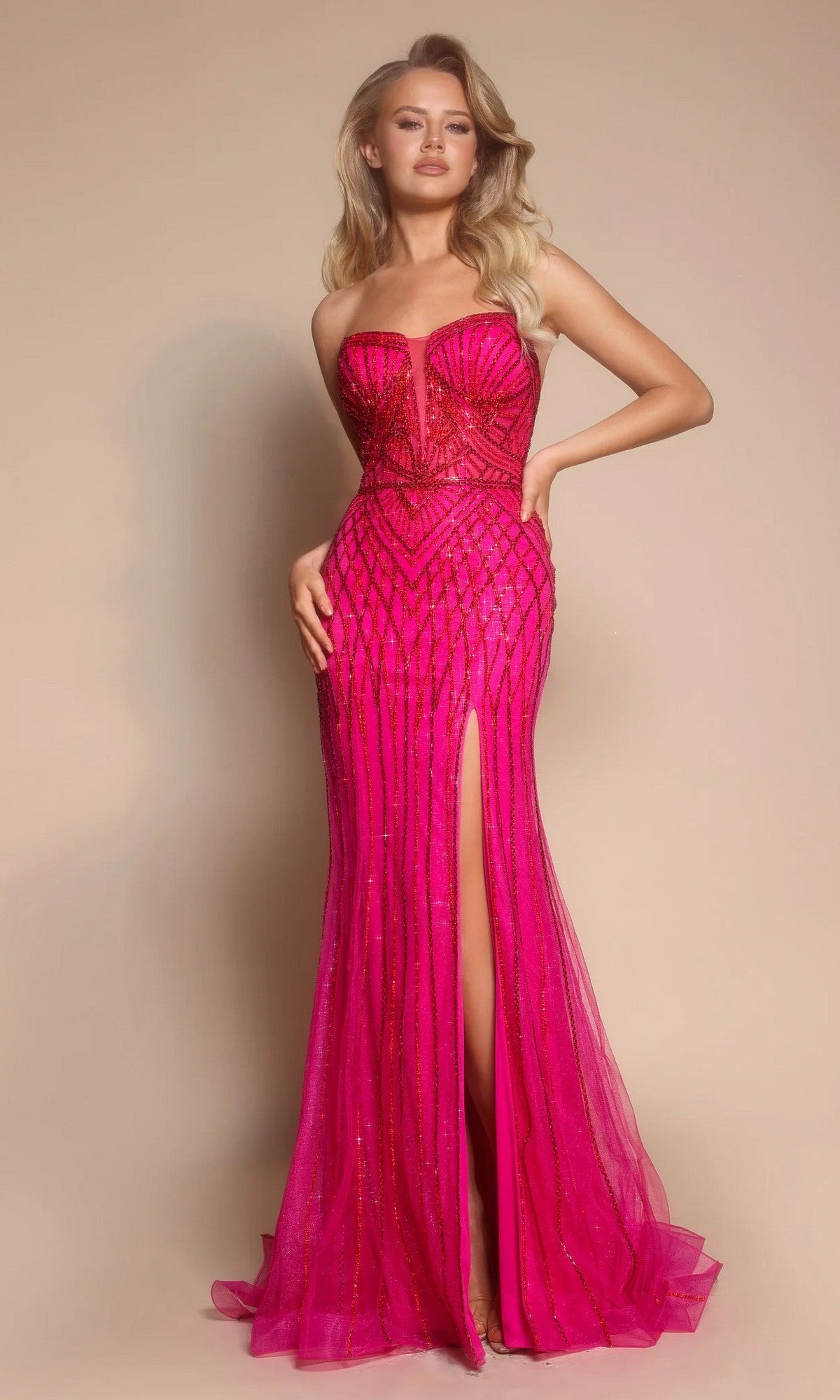 A woman wears the Portia and Scarlett PS26072 long formal dress in fuchsia, featuring a strapless embellished design with beaded details and a dramatic thigh-high slit, posed against a neutral background.